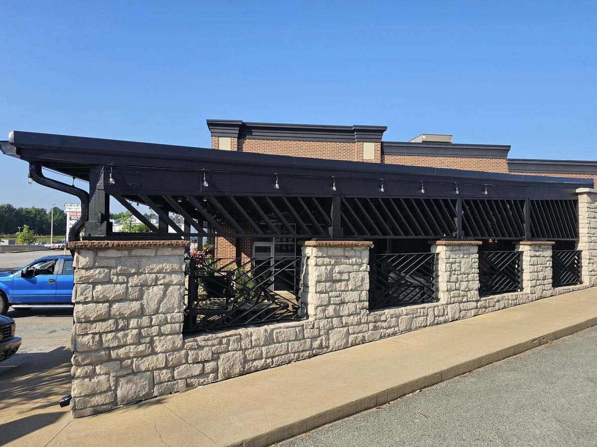 Black metal roof and gutter on a commercial patio structure with stone columns and iron railings.